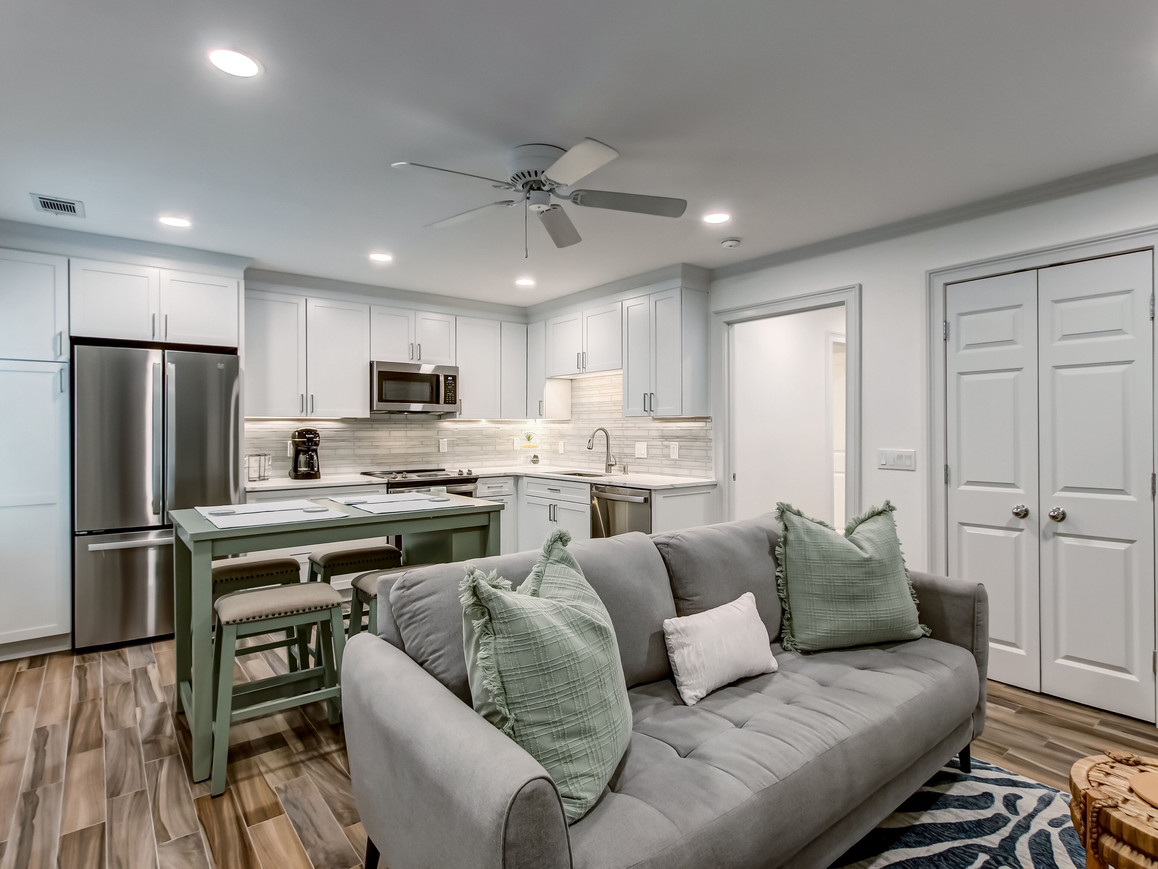 A modern kitchen with white cabinets, stainless steel appliances, and a dining area with a green table and bench.