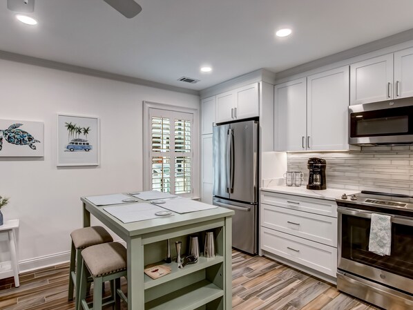 A modern kitchen with white cabinets, stainless steel appliances, and a dining area with a table and chairs. - Near Crawford Historic Square, Heated Pool Access (Savannah)