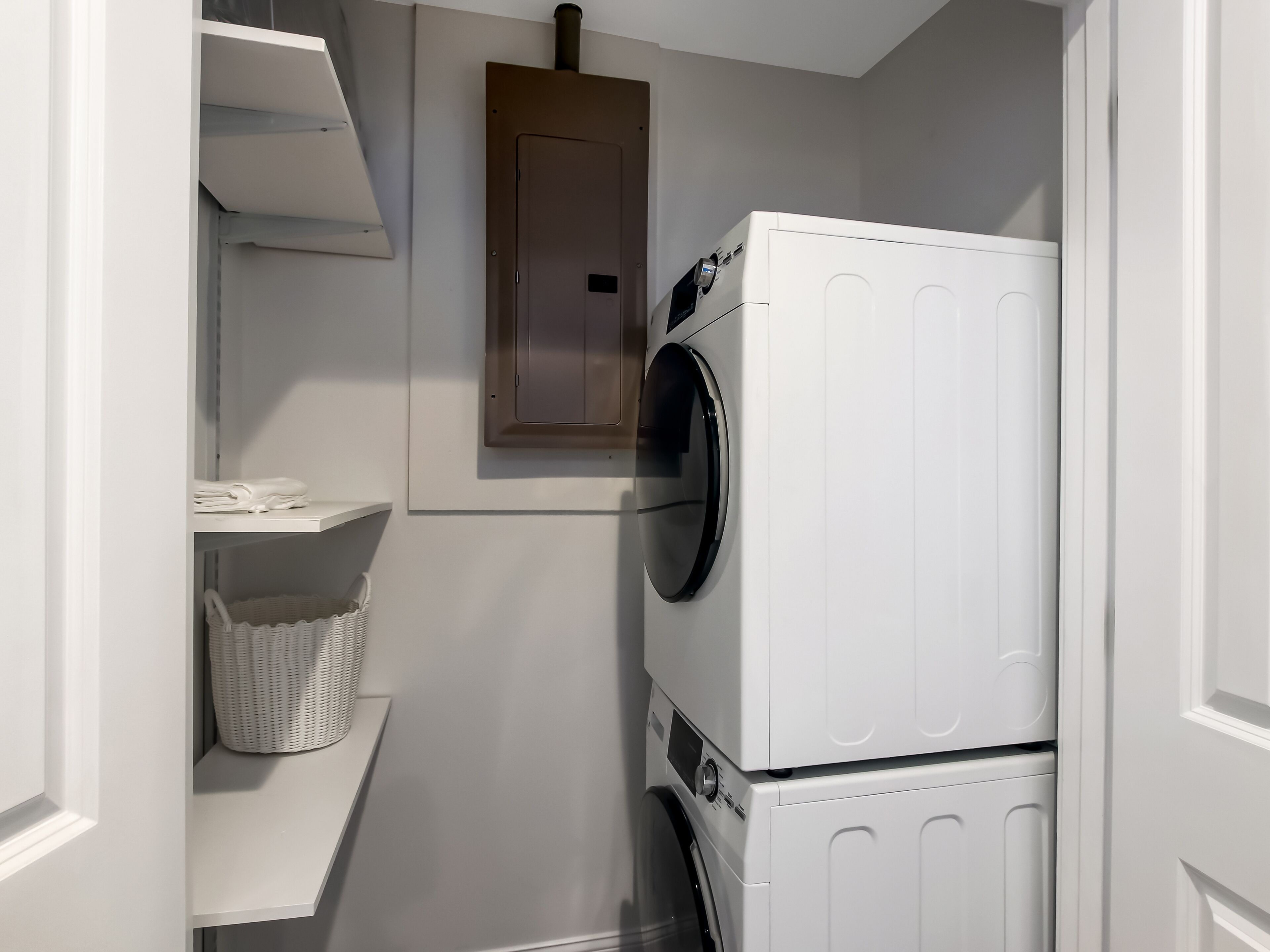 A compact laundry room with a stacked washer and dryer, a small shelf with folded towels, and a basket.