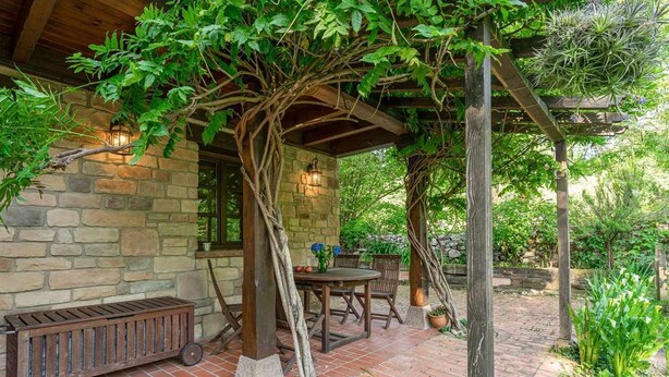 A covered patio with stone walls, wooden furniture, and a small table with a vase. - CASA ESCONDIDA CUENCU (Cuenco)
