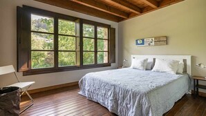 A bedroom with a large window, wooden flooring, a bed with white bedding, and a small bedside table. - CASA ESCONDIDA CUENCU (Cuenco)