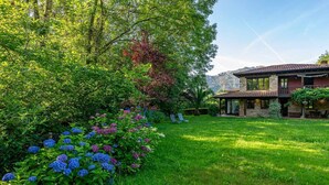 A house with a stone facade, a covered patio, and a lush garden with hydrangeas. - CASA ESCONDIDA CUENCU (Cuenco)