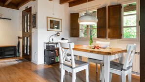 A kitchen with a wooden table, white chairs, a hanging light fixture, and wooden cabinets. - CASA ESCONDIDA CUENCU (Cuenco)