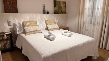 A neatly made bed with white linens and two rolled towels, a nightstand with a lamp, and a painting on the wall.