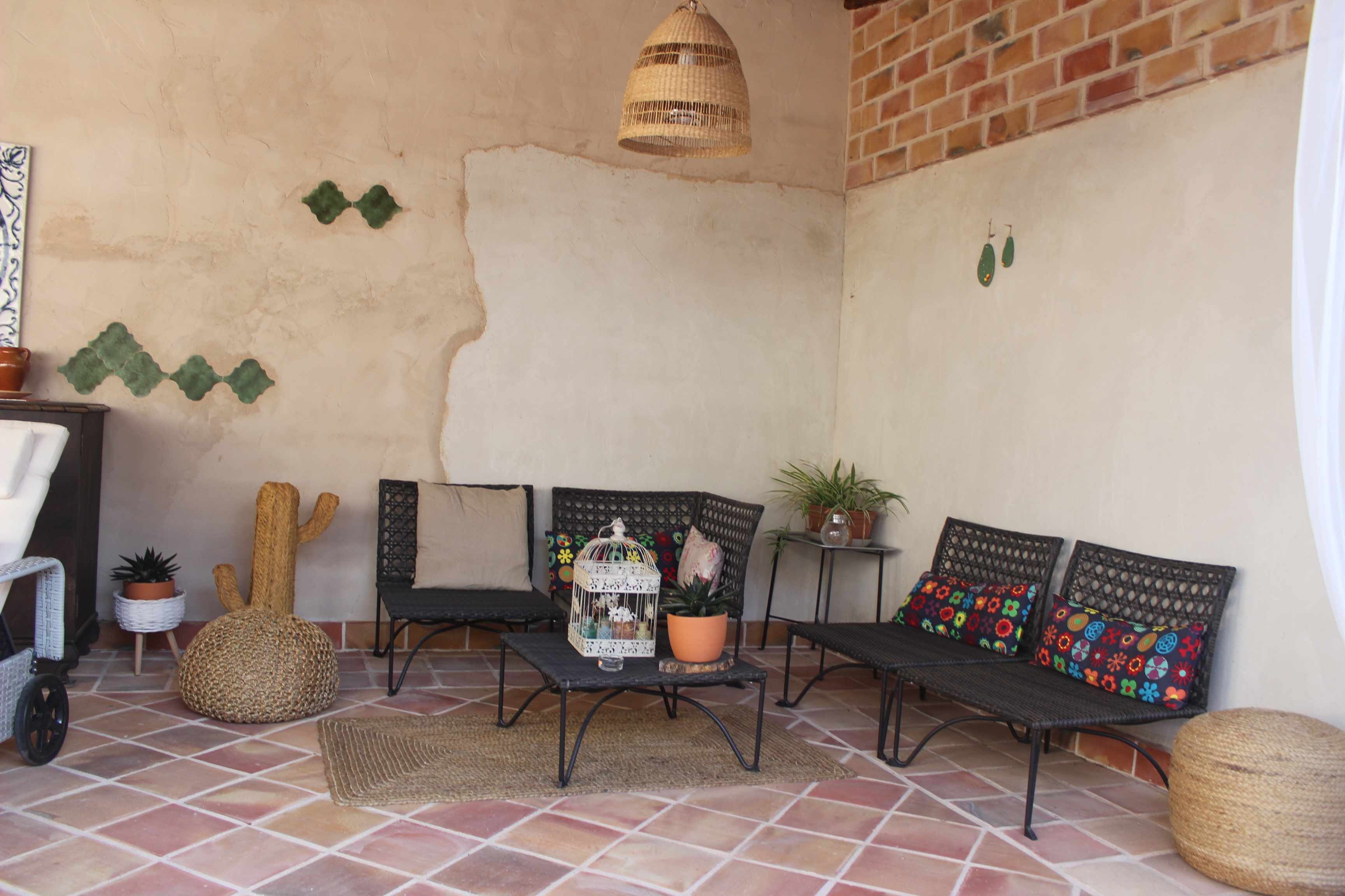 A cozy patio area with a woven bench, a small table with a birdcage, and potted plants.
