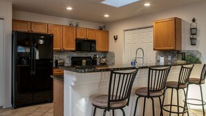 A kitchen with wooden cabinets, a black refrigerator, a microwave, a sink, and a bar area with stools. - La Shoshone Casita Rio (Lake Havasu City)