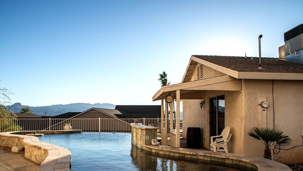 A swimming pool with a stone border, a covered patio area, and a view of mountains in the background. - La Shoshone Casita Rio (Lake Havasu City)