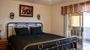 A bedroom with a metal bed frame, a ceiling fan, a framed picture on the wall, and a window with curtains. - La Shoshone Casita Rio (Lake Havasu City)