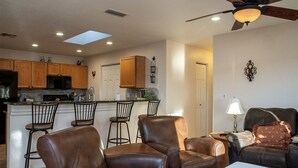 A modern kitchen with wooden cabinets, a bar area with stools, a ceiling fan, and a dining area with leather chairs. - La Shoshone Casita Rio (Lake Havasu City)