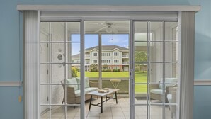 Une pièce dotée d’une porte-fenêtre coulissante qui donne sur une terrasse extérieure aménagée avec un canapé en osier, une petite table et une vue sur un immeuble à plusieurs étages en arrière-plan.