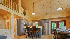 A spacious wooden cabin interior with a kitchen, dining area, and a loft bedroom. - Maplewood Haven | HOT TUB, Outdoor TV, Turf + Patio! (Broad Top)