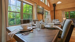 A wooden dining table set for four with a television mounted on the wall above. - Maplewood Haven | HOT TUB, Outdoor TV, Turf + Patio! (Broad Top)