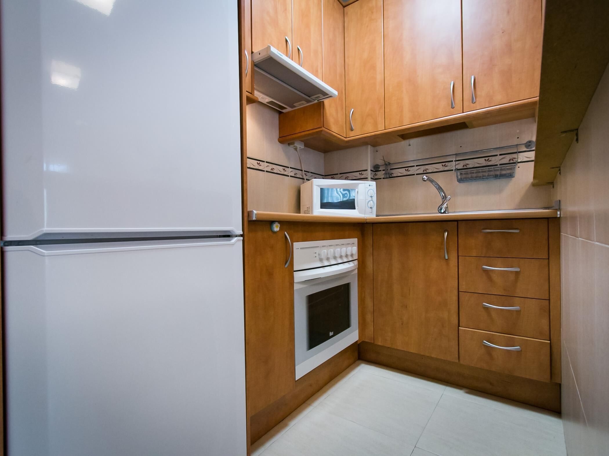 Una cocina compacta con armarios de madera, un refrigerador blanco, un microondas y un horno.