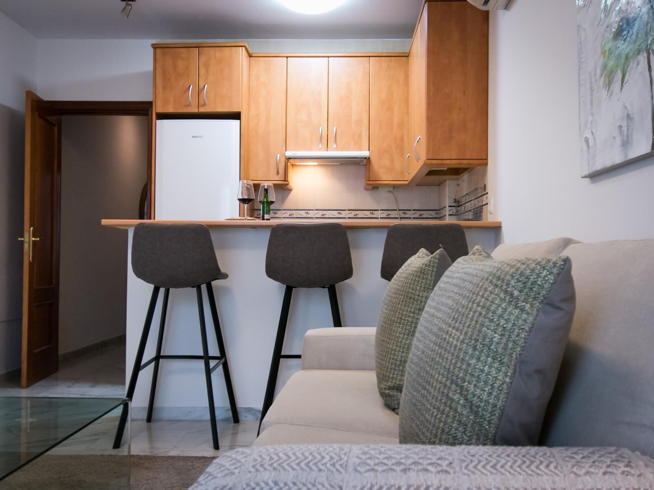 A compact kitchen with wooden cabinets, a white refrigerator, and a bar stool.