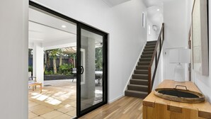 A modern interior with a wooden floor, a staircase, and a glass door leading to an outdoor area with a patio and plants. - Central Tropical Oasis with Pool - Pet Friendly (Noosaville)