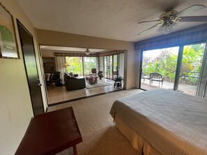A bedroom with a large bed, a desk, and a balcony with outdoor furniture. - Molokai condo Pool/Spa, 2 bedrooms/2 bathrooms. Walking distance to the beach. (Maunaloa)