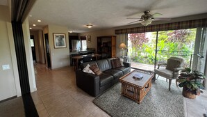 A spacious living room with a black leather sofa, a coffee table, and a dining area with a kitchen in the background. - Molokai condo Pool/Spa, 2 bedrooms/2 bathrooms. Walking distance to the beach.  (Maunaloa)