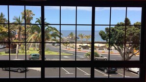 Blick durch ein Fenster mit Gittermuster, zeigt einen Parkplatz, Palmen und einen strahlend blauen Himmel.