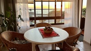 Ein Essbereich mit Korbstühlen, einem weißen Tisch und Blick auf den Sonnenuntergang durch große Fenster.