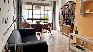 Ein Wohnzimmer mit einer Couch, Korbstühlen, einem runden Tisch, einer TV-Konsole und einem Fenster mit Vorhängen.