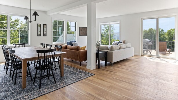 Un espacio habitable amplio con una mesa de comedor y sillas, un sofá, y un gran ventanal corredero que da a un patio exterior.
