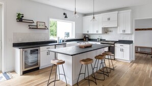 Una cocina moderna con armarios blancos, una isla central con taburetes, horno empotrado e iluminación colgante.