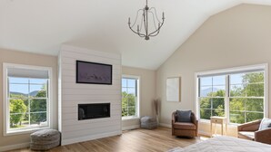 Un dormitorio amplio con una cama grande, una chimenea y varias ventanas que ofrecen vistas a la vegetación y montañas.