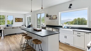 Una cocina moderna con una isla central, taburetes de bar y un amplio ventanal con vistas al exterior.
