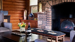 A cozy log cabin interior with a stone fireplace, a dining table with wine glasses and a vase of flowers, and a comfortable seating area.