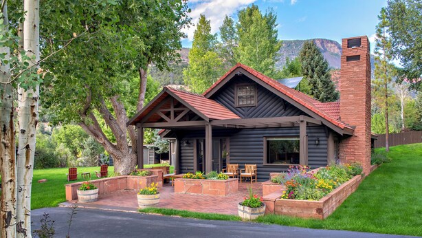 A log cabin with a covered porch, outdoor seating, and a brick chimney.