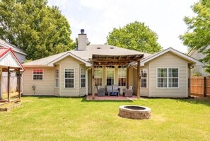 A two-story house with a covered patio area and a fire pit in the backyard.