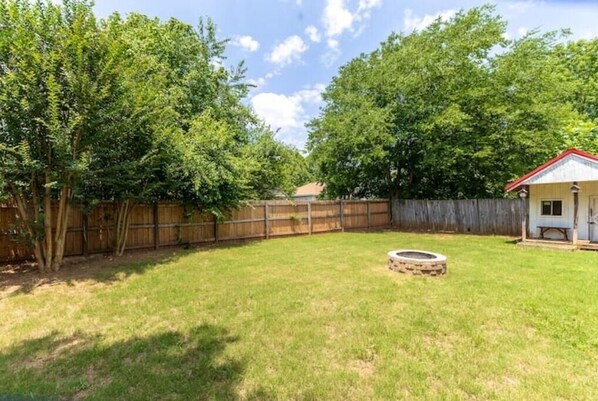 A backyard with a wooden fence, a small circular fire pit, and a wooden structure with a red roof.