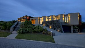 A modern house with a stone facade, a staircase leading to the entrance, and a well-maintained lawn. - Mt Gold Retreat - Tennis court - Hot Tub (Wanaka)