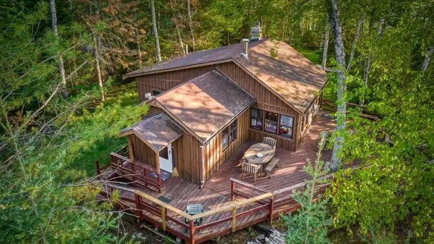Eine Hütte mit einer Terrasse, einem Kamin und einem großen Fenster mit Blick auf den Wald.