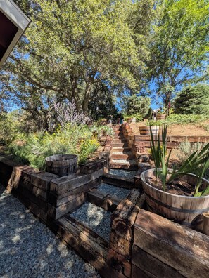 A garden with a wooden staircase leading up to a structure, surrounded by various plants and trees.