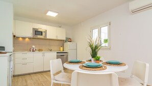 Eine moderne Küche mit weißen Schränken, einer Mikrowelle und einem Kühlschrank. Ein Esstisch mit vier Stühlen und einem Blumentopf sind ebenfalls vorhanden.