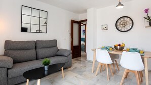 A modern living room with a grey sofa, a black coffee table, and a dining area with a wooden table and white chairs.
