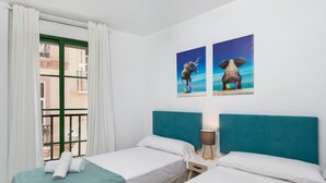 A hotel room with two beds, a window with curtains, and two wall-mounted paintings of elephants.