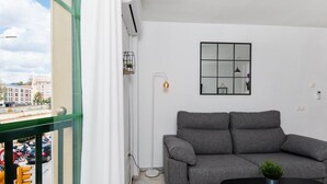 A modern living room with a grey sofa and a black coffee table, a small potted plant, and a view of the city through a large window.