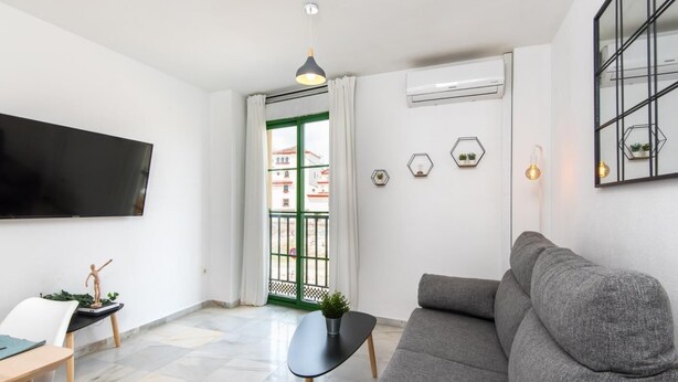 A modern living room with a grey sofa, a flat-screen TV, a small table with a plant, and a view through a green door to the outside.