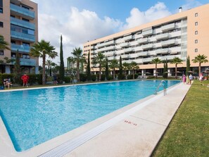 A swimming pool surrounded by palm trees and a multi-story building with balconies.
