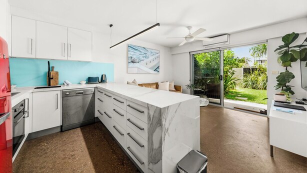 A modern kitchen with white cabinets, a marble island, and a large window overlooking a garden. - 5 mins walk to Hastings Street (Noosa)