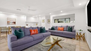 Una sala de estar moderna con dos sofás, una mesa de centro de vidrio y una zona de comedor con sillas.