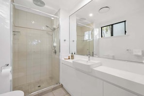 Un bagno moderno con doccia vetrata, uno specchio grande e un lavandino bianco.