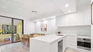 Una cocina moderna con armarios blancos, una isla central y un comedor con sillas.