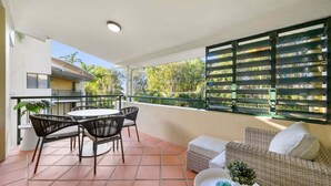 Un patio cubierto al aire libre con una mesa y sillas de comedor, un sofá de mimbre y una barandilla con listones horizontales.