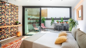 Ein modernes Schlafzimmer mit einem großen Bett, einer Glastür zum Balkon und einem Essbereich mit Topfpflanzen.
