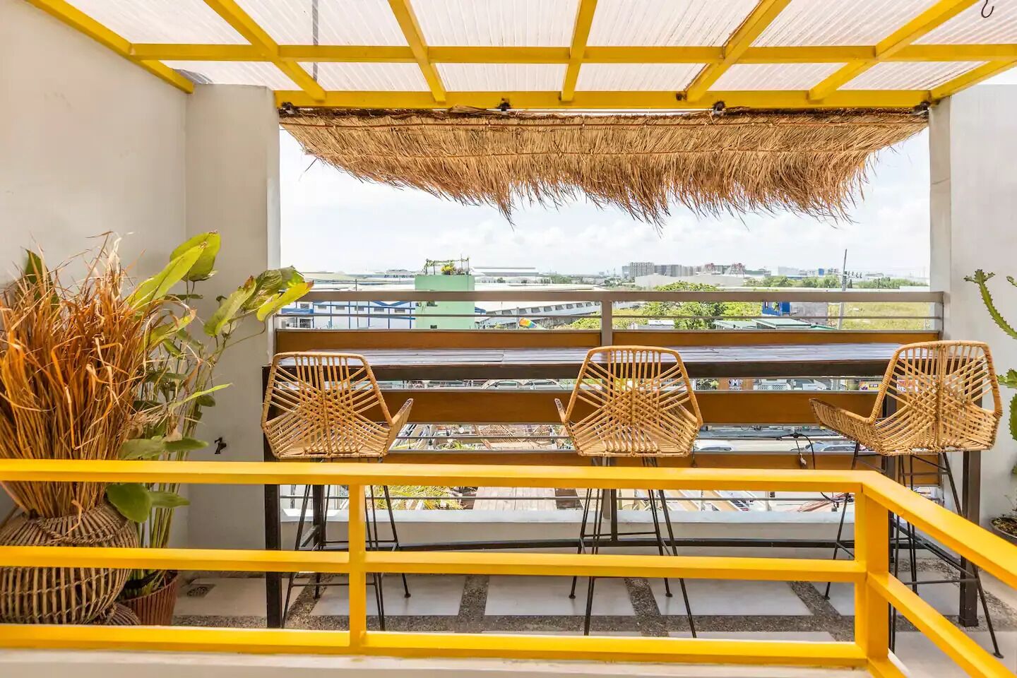 A balcony with a yellow railing, wicker chairs, and a thatched roof.