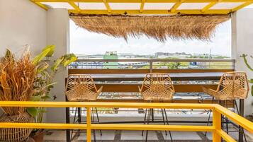 A balcony with a yellow railing, wicker chairs, and a thatched roof.