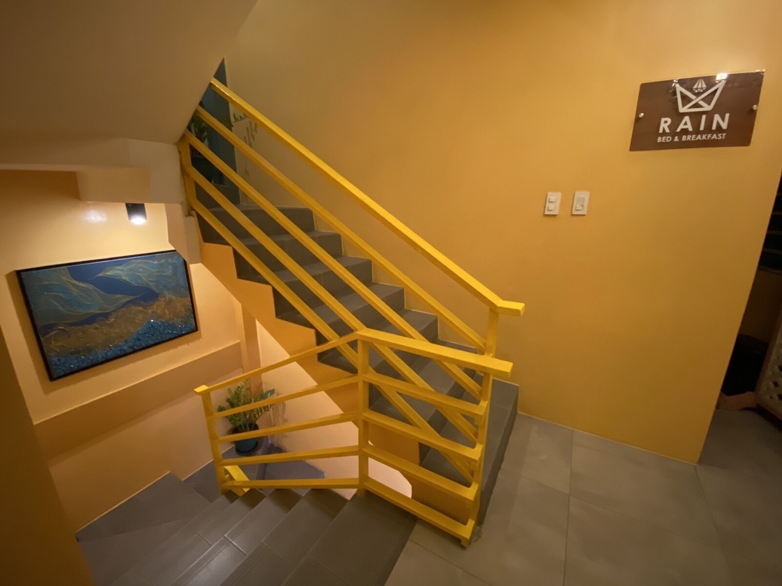 Eine Treppe mit gelben Geländern, ein Bild an der Wand und ein Schild mit der Aufschrift 'RAIN BED & BREAKFAST'.
